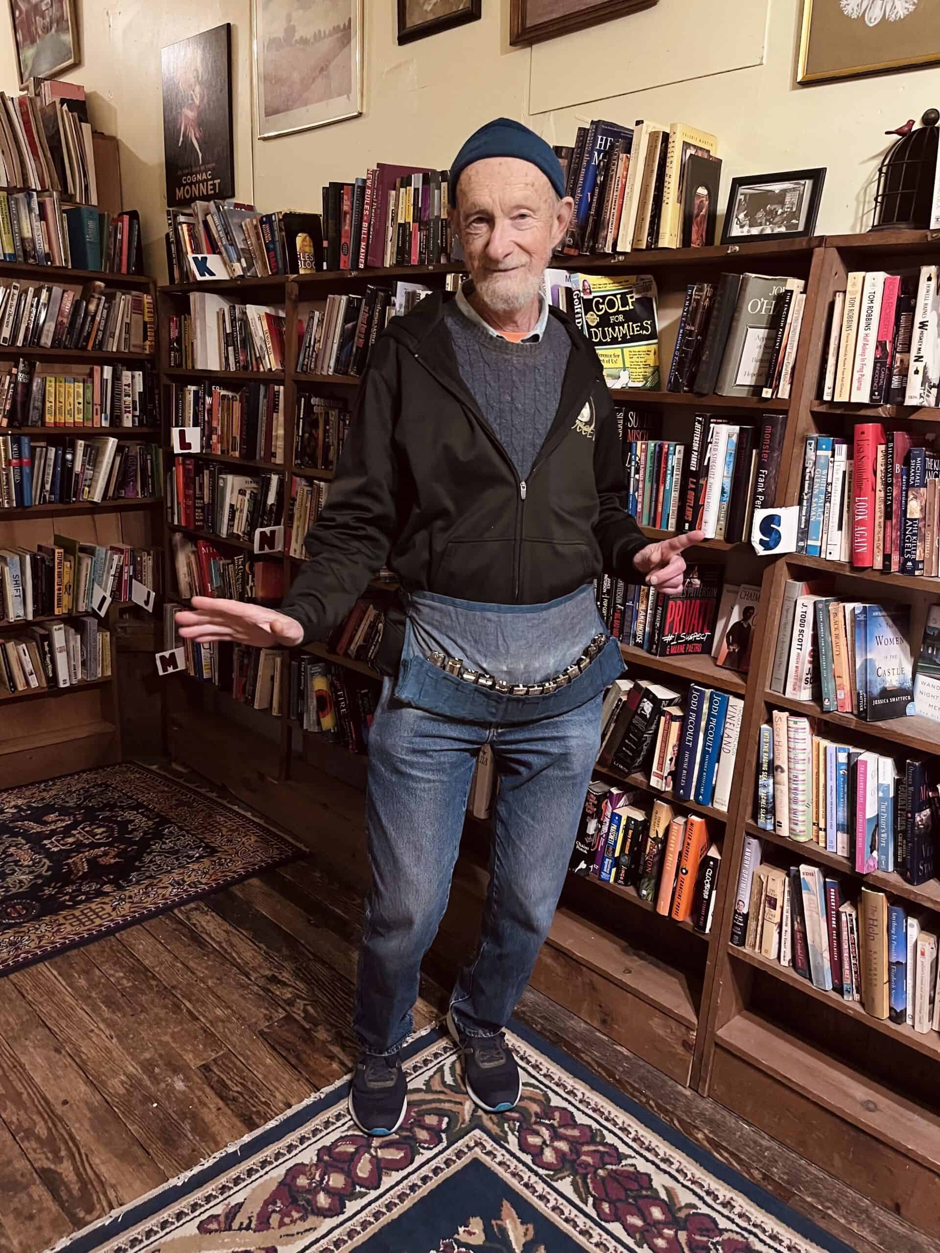 Man in a bookstore with shelves of books in the background.