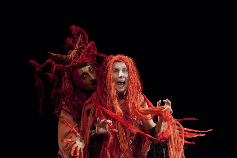 Theatrical performance with two actors in vibrant costumes and dreadlocks on stage.