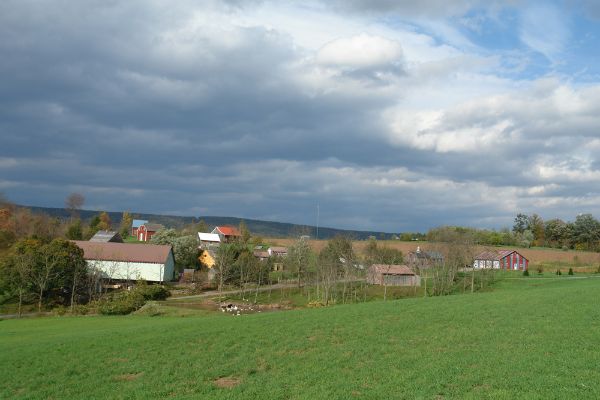 Scenic view of a rural community with houses and green fields under a cloudy sky.