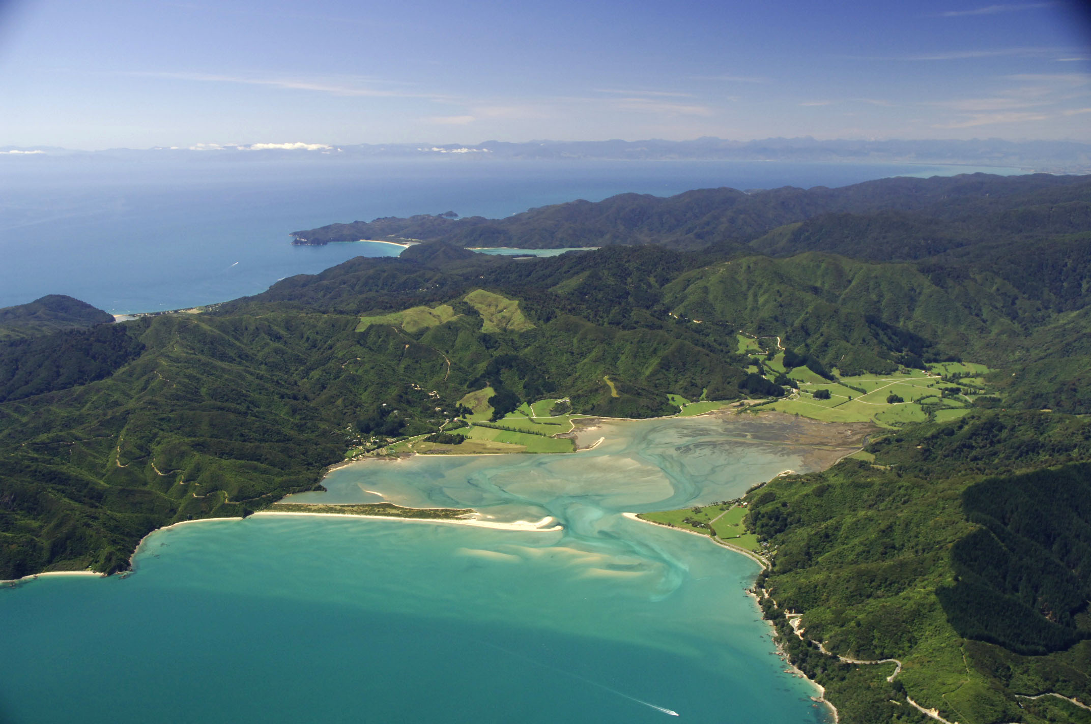 Aerial view of lush green hills and turquoise waters at Tui Community, New Zealand.