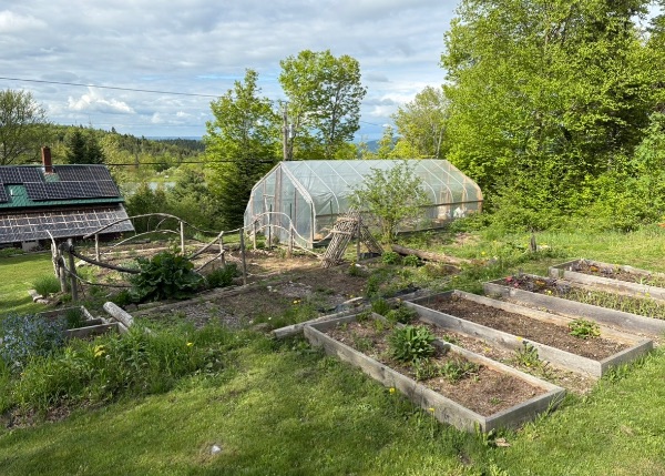 Community garden with raised beds, greenhouse, and solar panels in a rural setting.