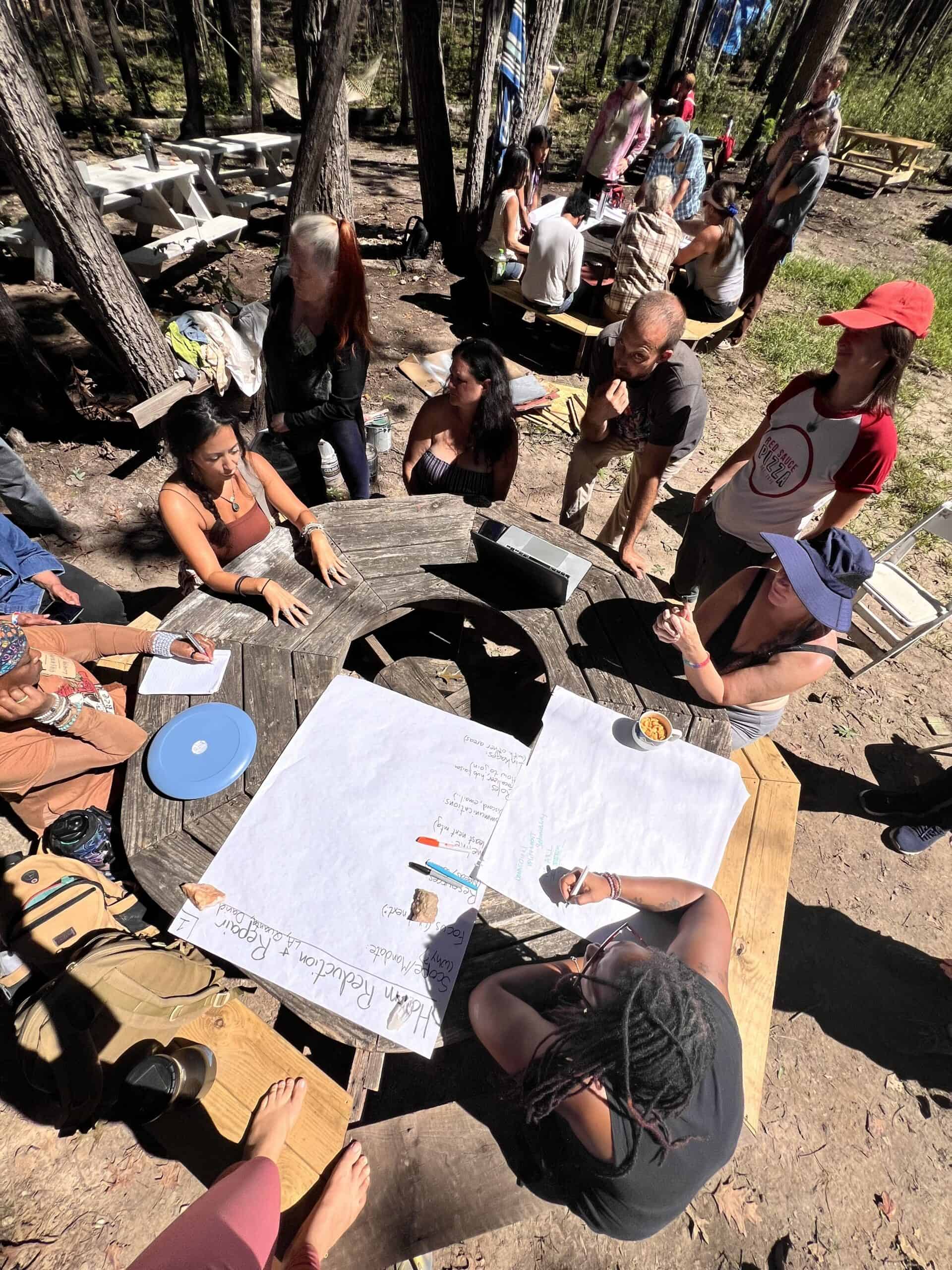 People gathered around a wooden table outdoors during a community event.