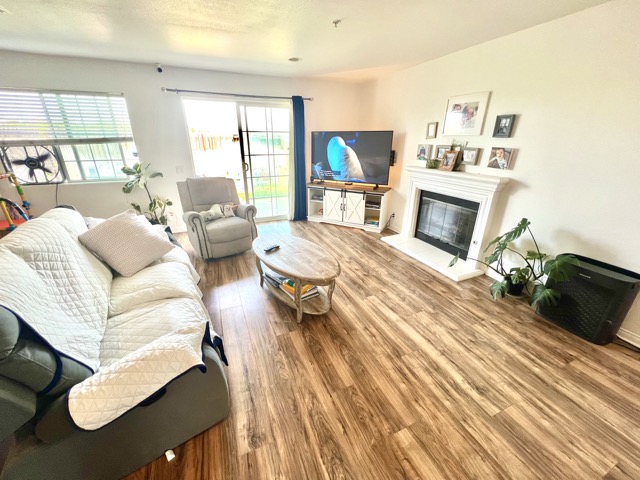 Bright living room with white sofa, armchair, and fireplace, hardwood floors, and large windows.