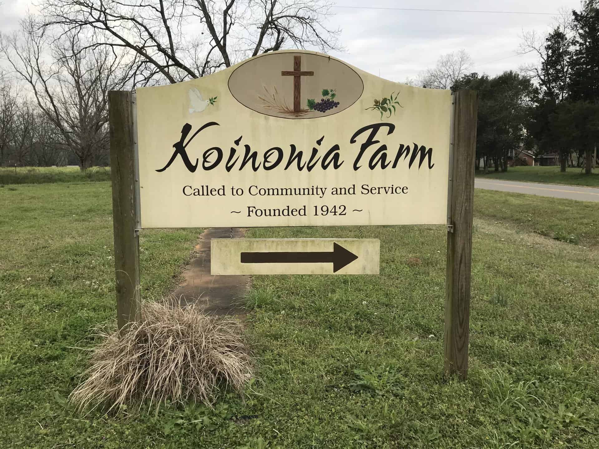Sign for Koinonia Farm with cross and arrow pointing right.