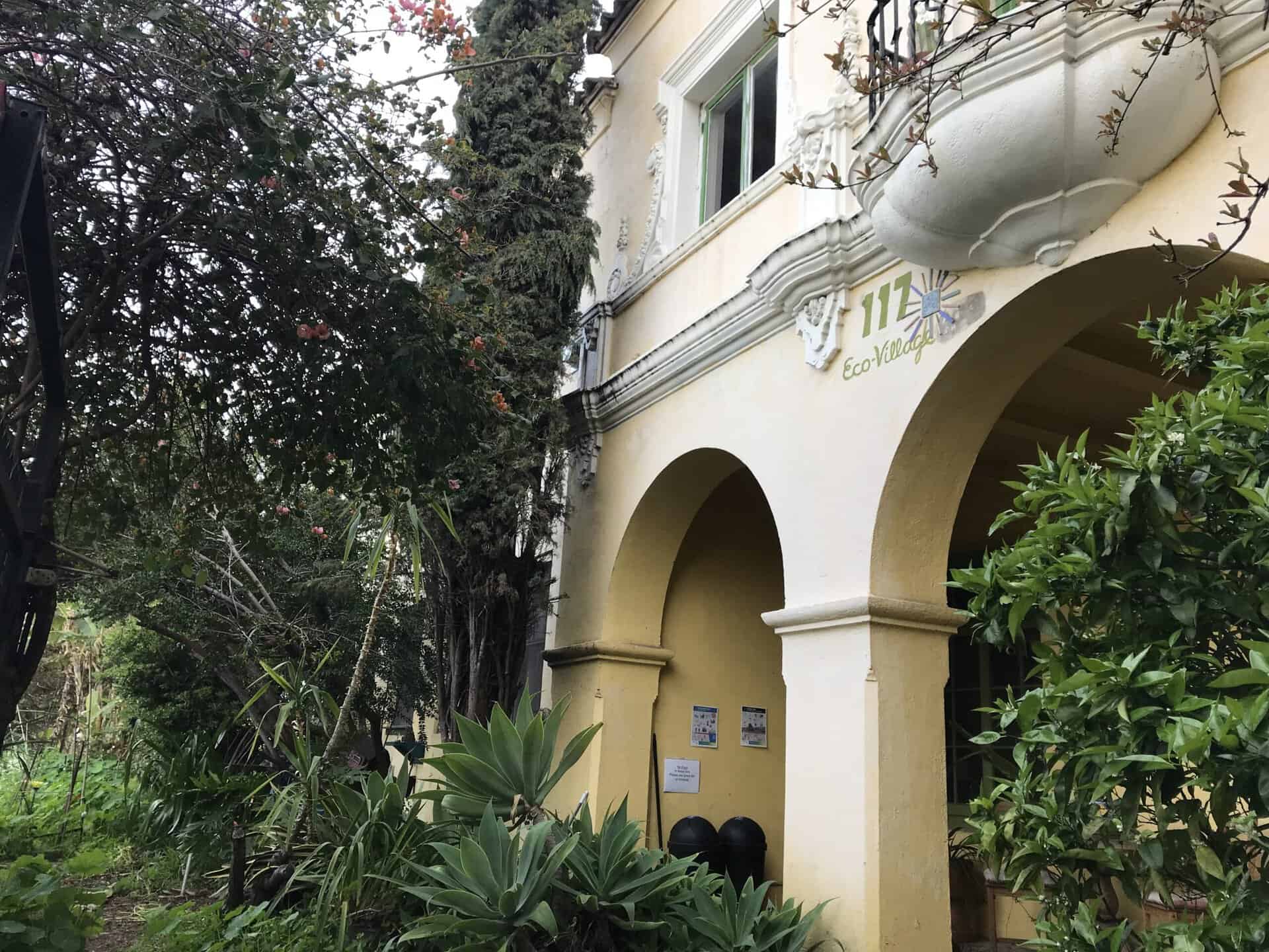 Exterior view of Los Angeles Eco-Village with lush greenery and white building.