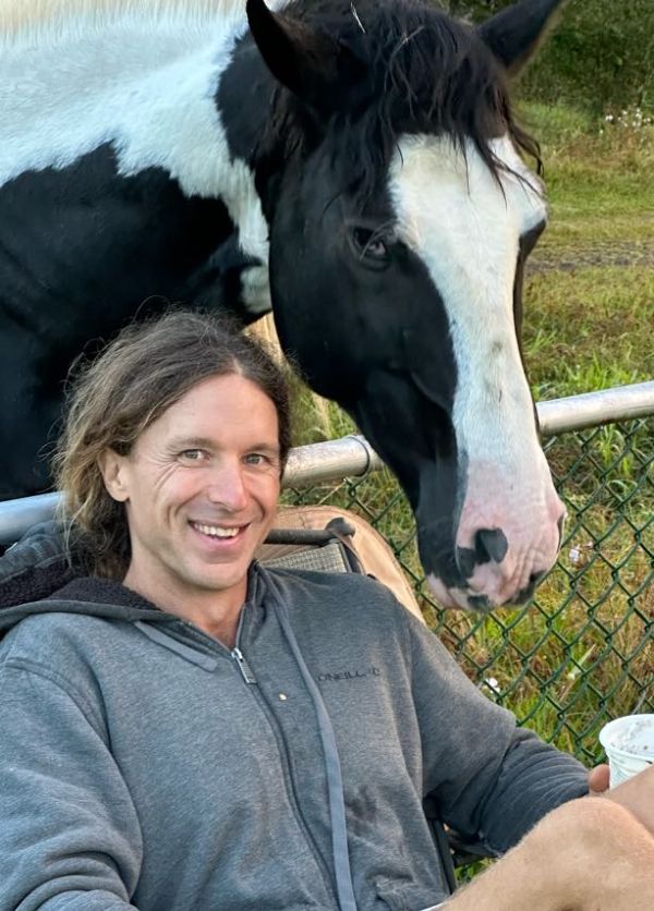 Person smiling with a black and white horse outdoors near a fence.