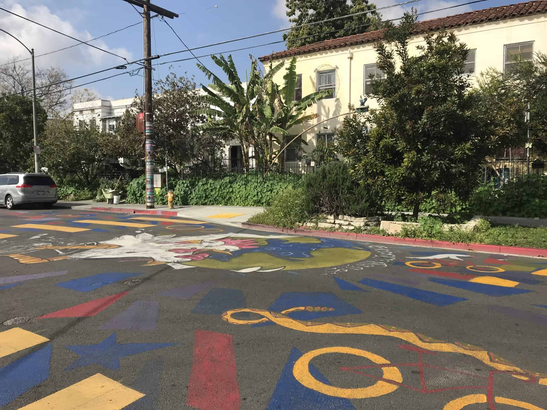Colorful street mural with community and environmental themes in front of residential buildings.
