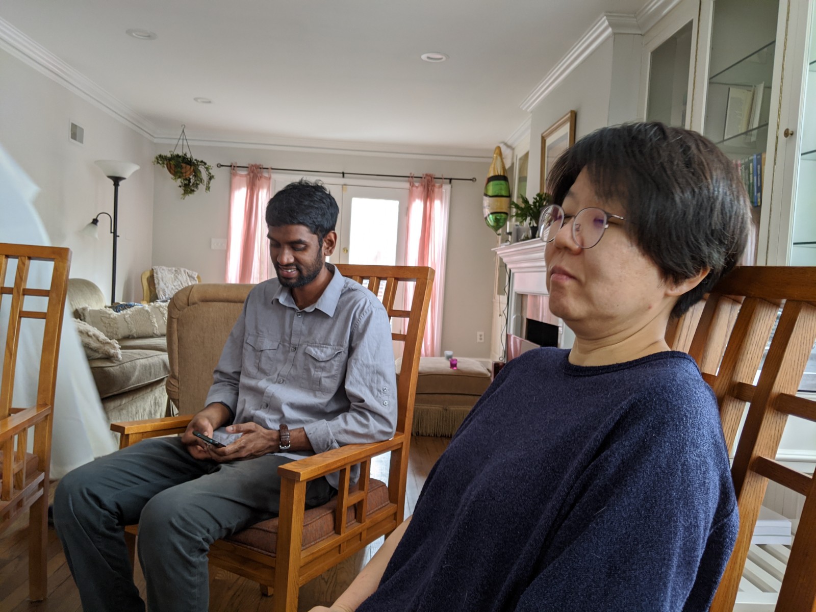 People sitting in a cozy living room with wooden chairs and soft lighting.