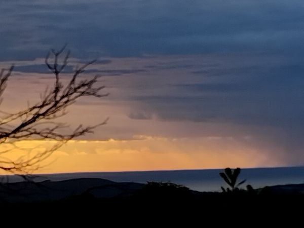 Sunset over a landscape with silhouetted trees and distant hills.