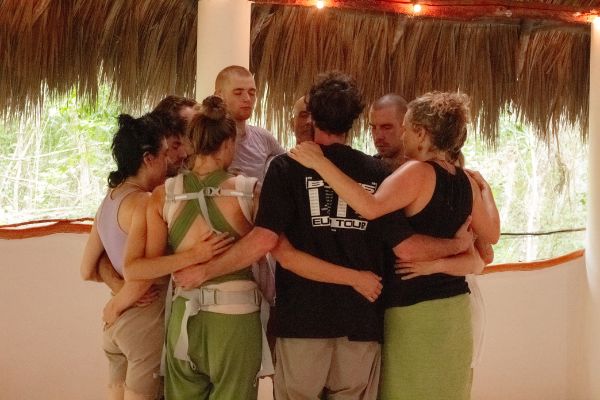 Group of people in a circle embracing in a tropical setting.