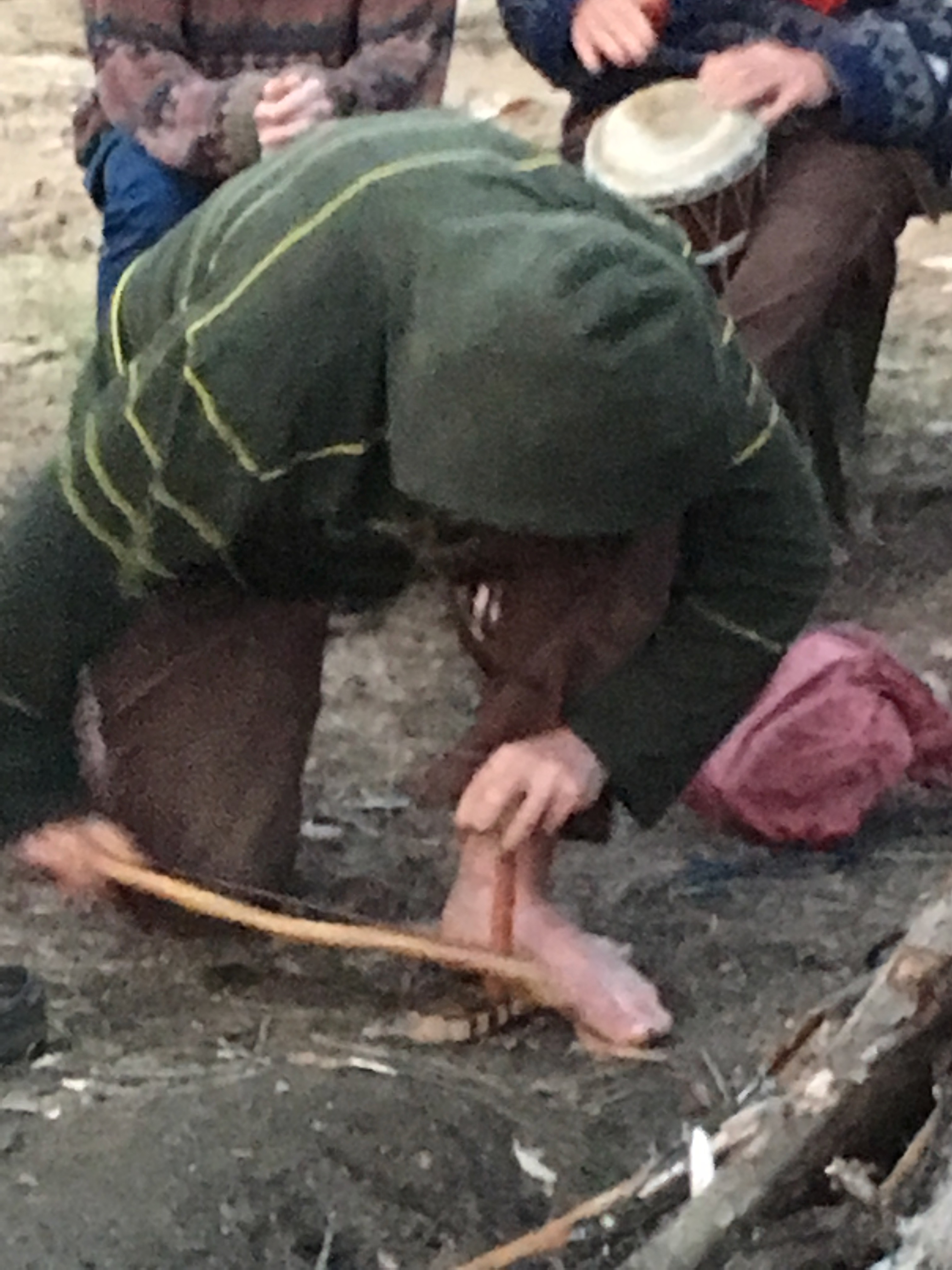 Person preparing a fish over an open fire in an outdoor setting.