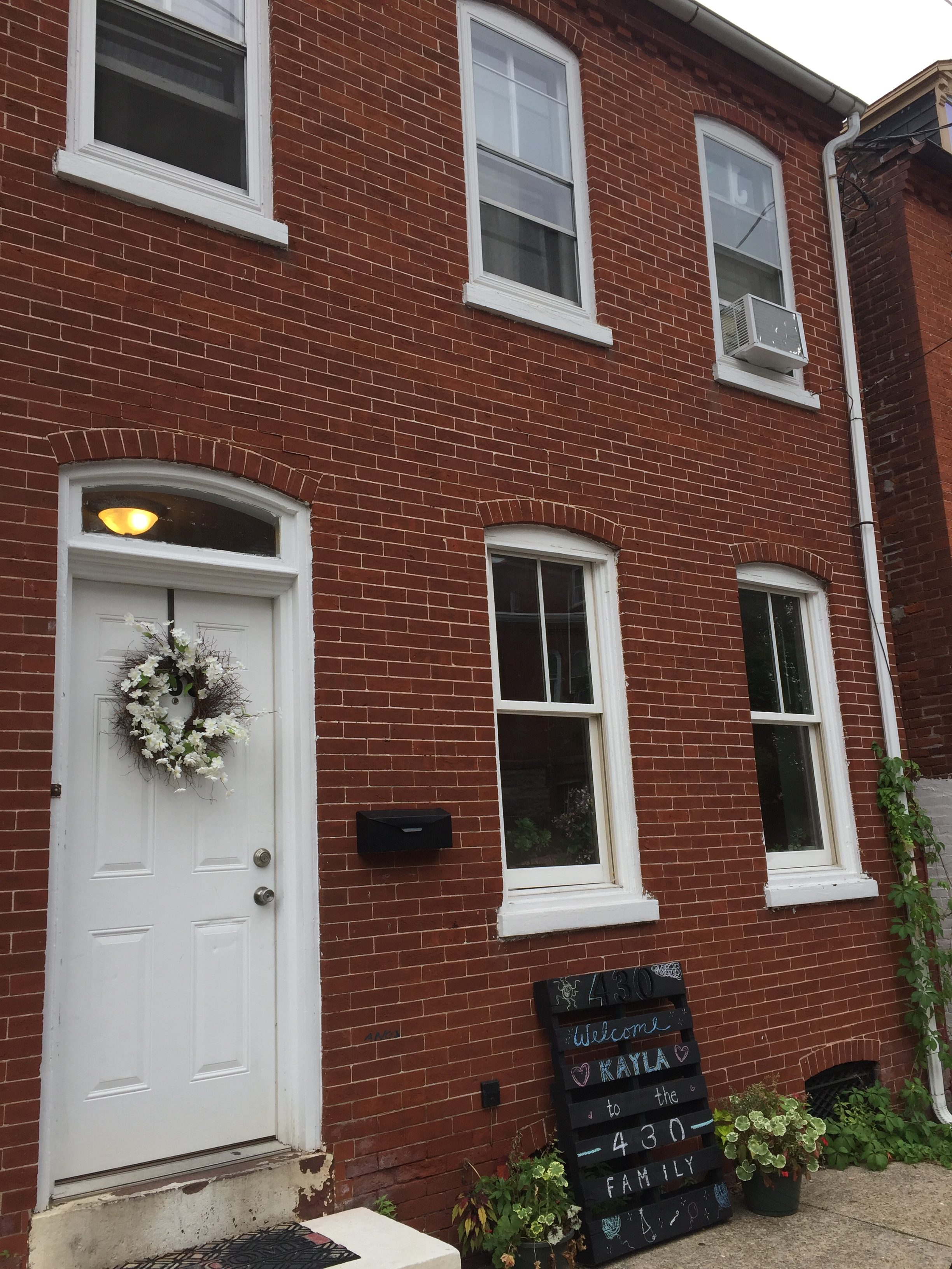 Brick townhouse with white door and welcoming sign for family and friends.