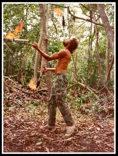Person chopping wood in a forest, surrounded by trees and fallen leaves.