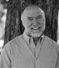 Smiling man outdoors with trees in background, professional portrait.