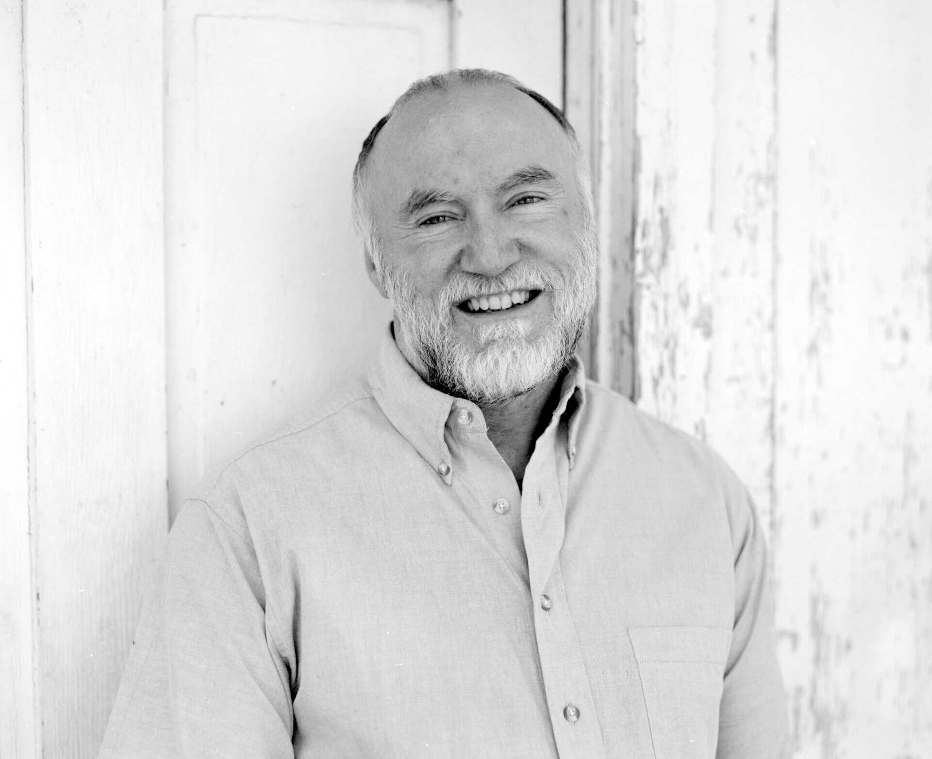 Smiling older man with a beard in a casual shirt, black and white photo.