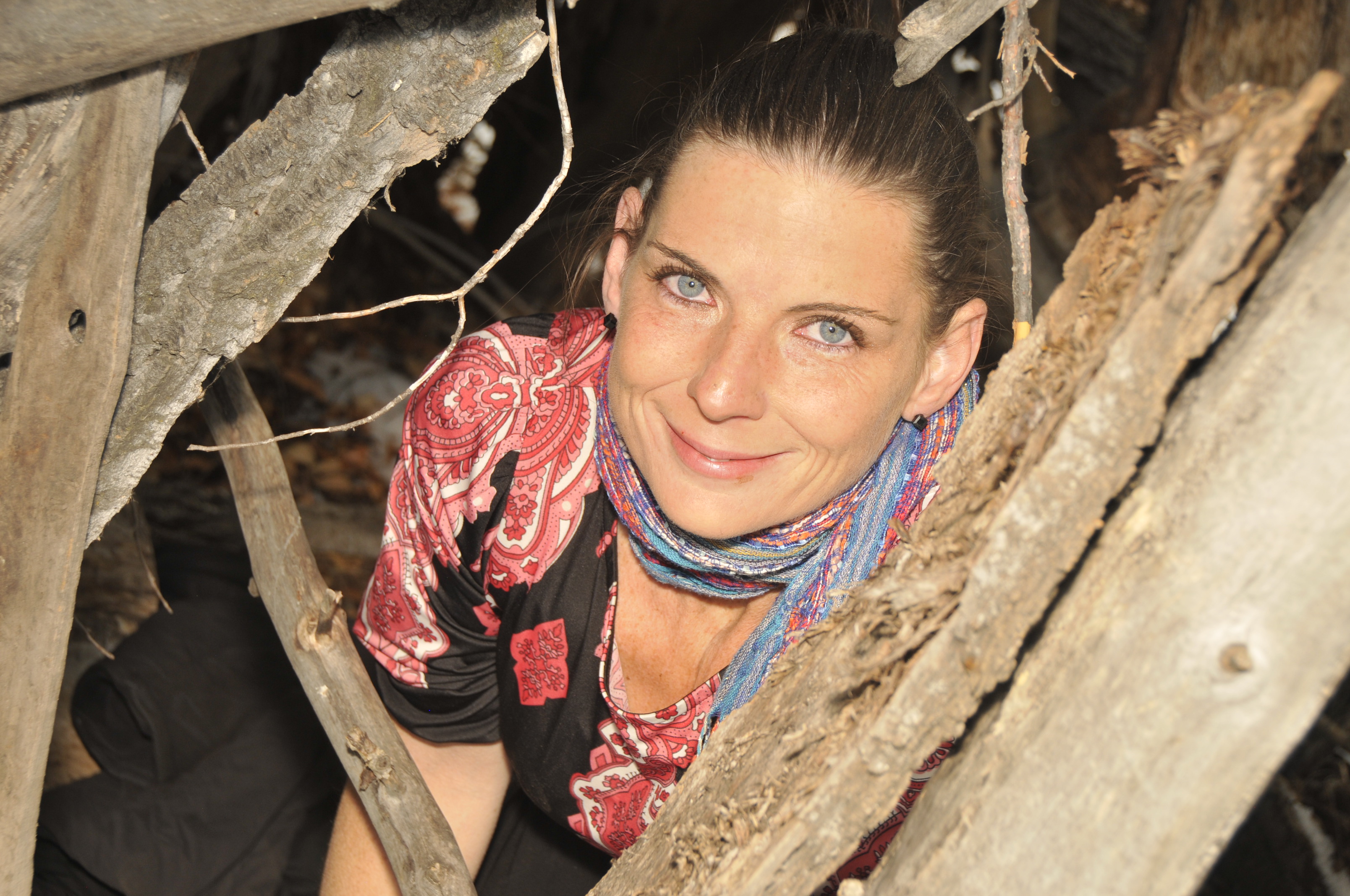 Woman smiling in a forest among tree branches and logs.