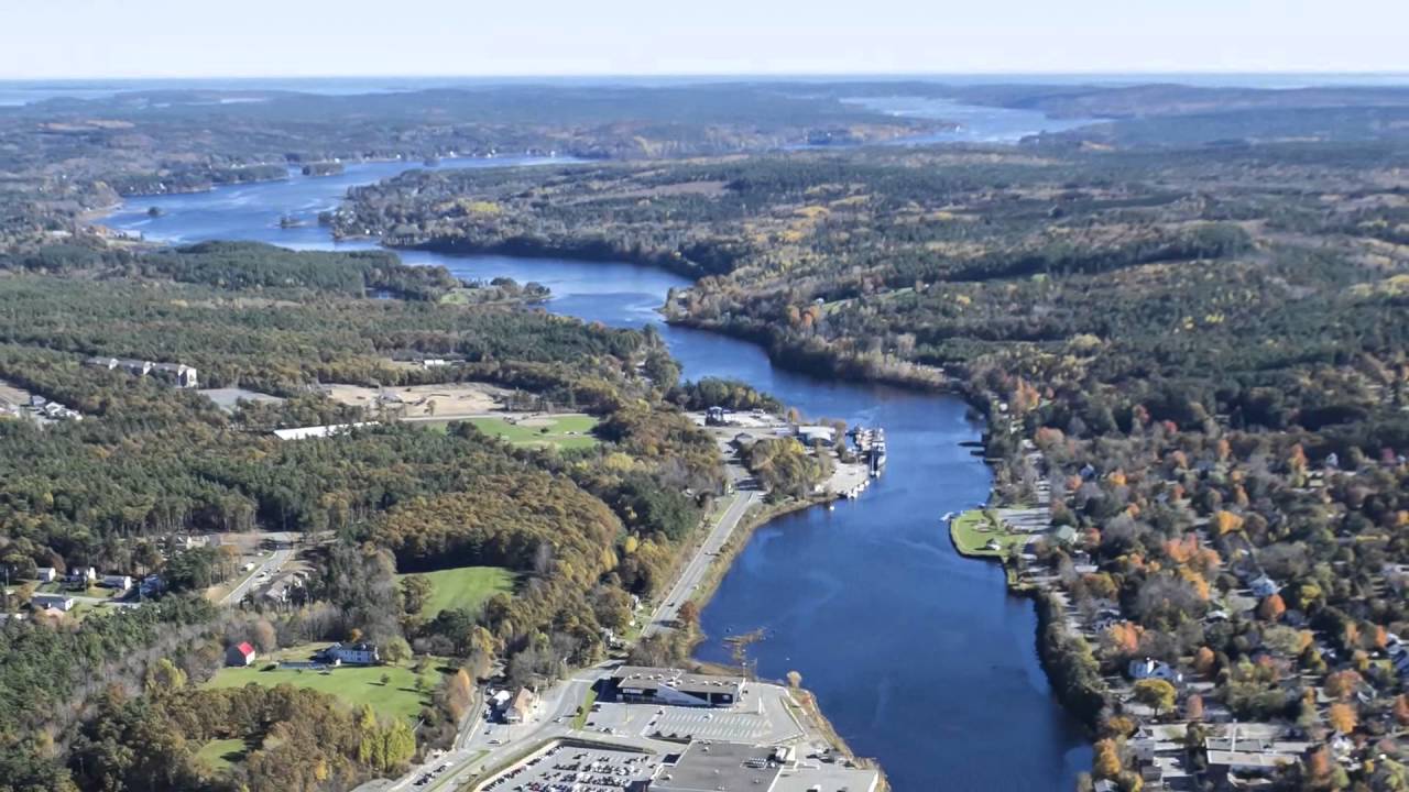 Aerial view of a river flowing through a lush green landscape with houses and forests.