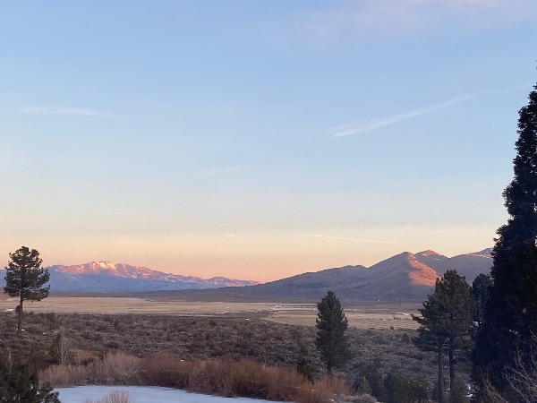Scenic view of mountains, trees, and open land at sunset.