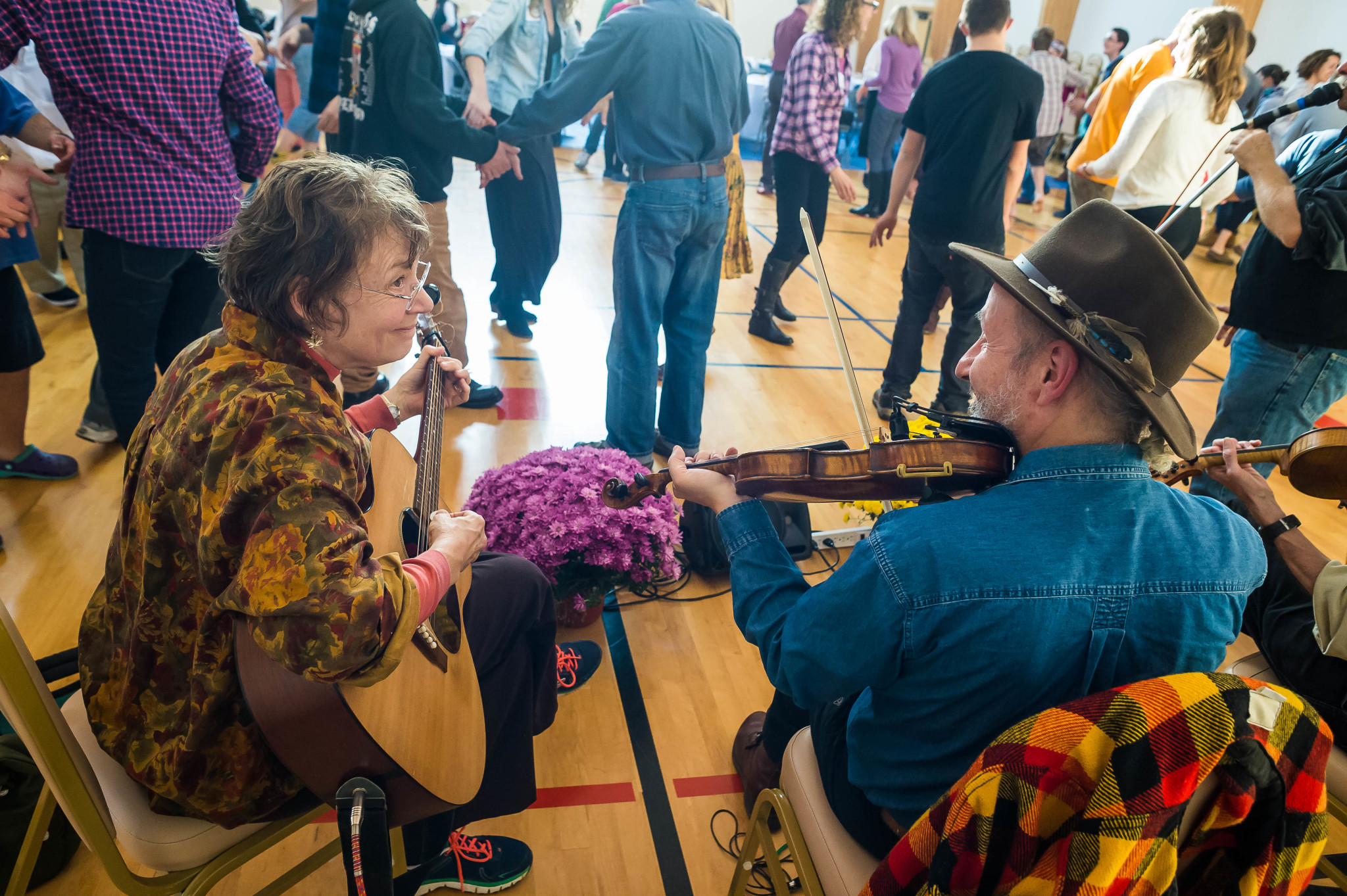 People playing guitar and violin at a community event in a gymnasium.