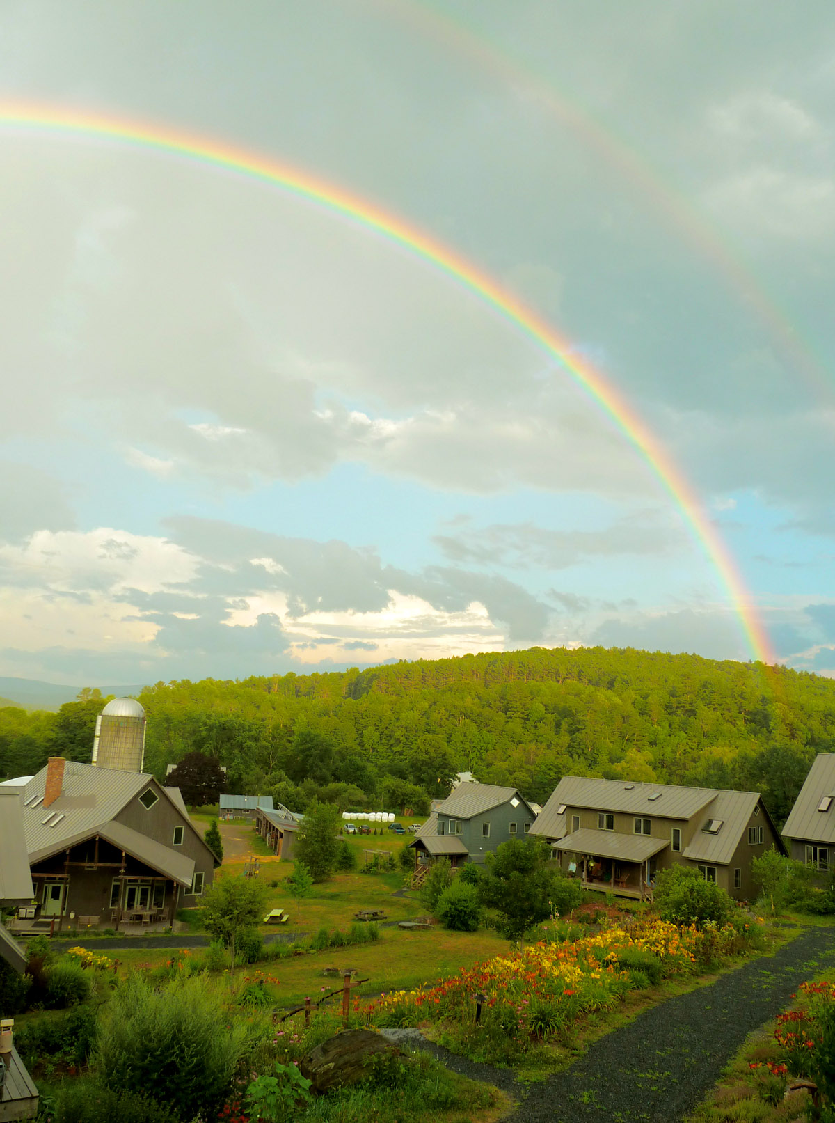 Rainbow over a peaceful community with houses and lush greenery.