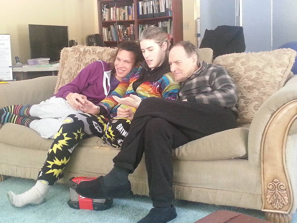 Three people sitting on a beige couch, smiling and looking at a phone.