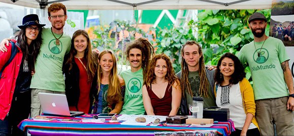 Diverse group of people at an outdoor community event with a table and green plants.