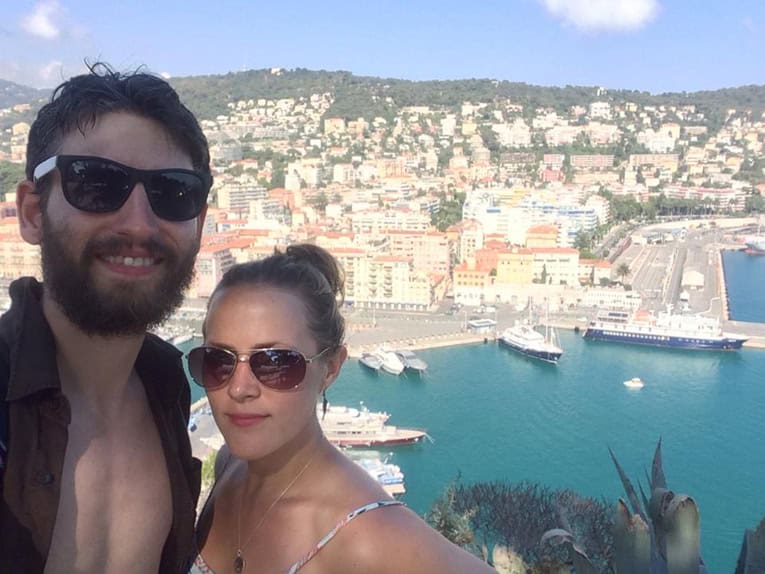 Couple enjoying a scenic harbor view with boats and cityscape in the background.