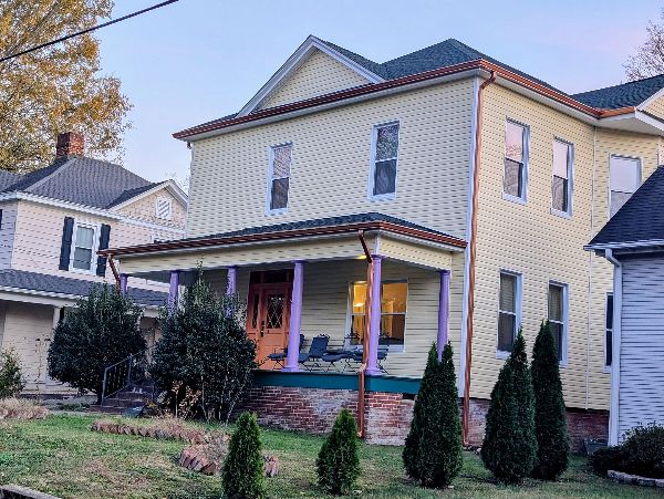 Yellow two-story house with front porch and landscaped yard in a neighborhood.