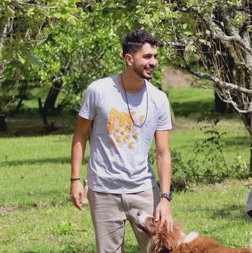 Young man smiling outdoors with a dog in a green park setting.