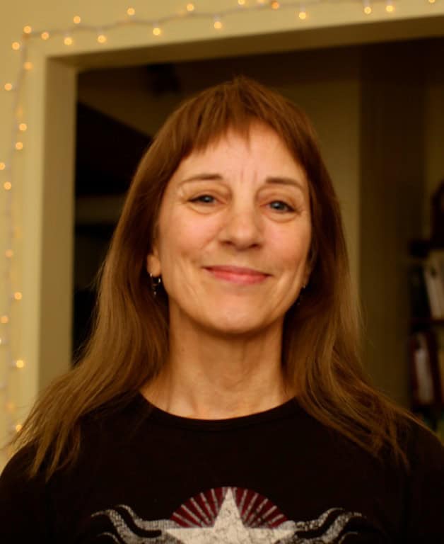 Portrait of a smiling woman with long brown hair in a cozy indoor setting.