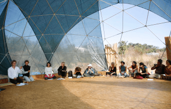 Group of people sitting in a semi-circle inside a geodesic dome.