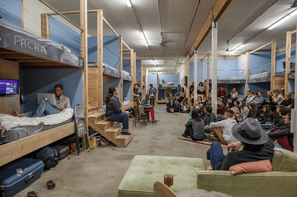 People gathered in a communal space with bunk beds and seating areas.
