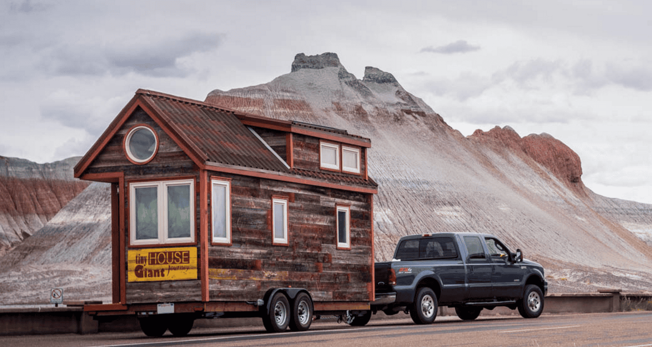 Unique tiny house on wheels parked in a rugged landscape with mountains.