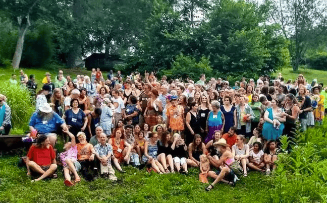 Large group of people gathered outdoors in a lush green setting.