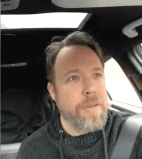 Man with beard driving a car, looking out the window.
