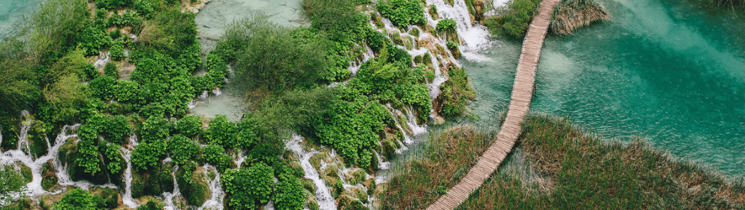 Lush green landscape with waterfalls and a winding path near a river.