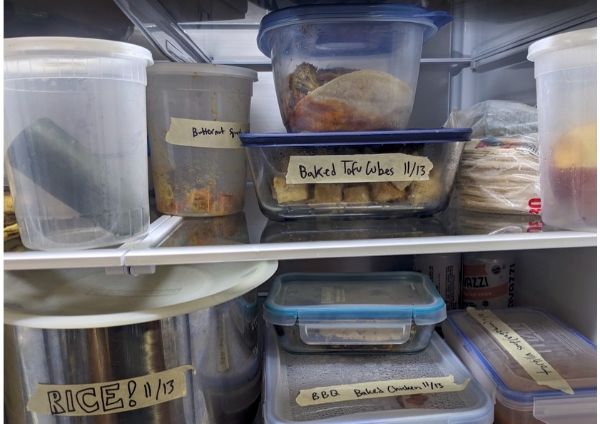 Organized refrigerator with labeled containers of baked tofu cubes, rice, and BBQ chicken.