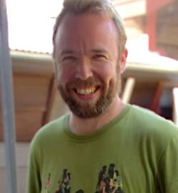 Smiling man with a beard wearing a green T-shirt outdoors.