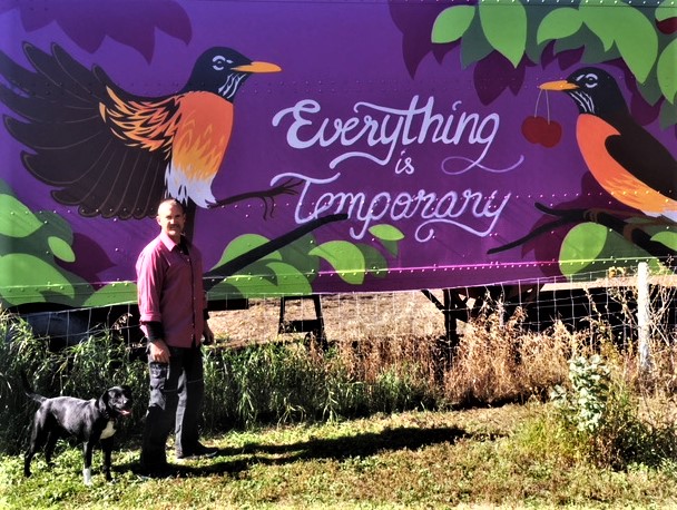 Person with dog standing in front of colorful mural with birds and the phrase "Everything is Co-Oper.