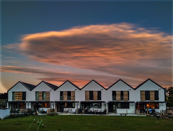Modern cohousing homes with gabled roofs under a colorful sunset sky.