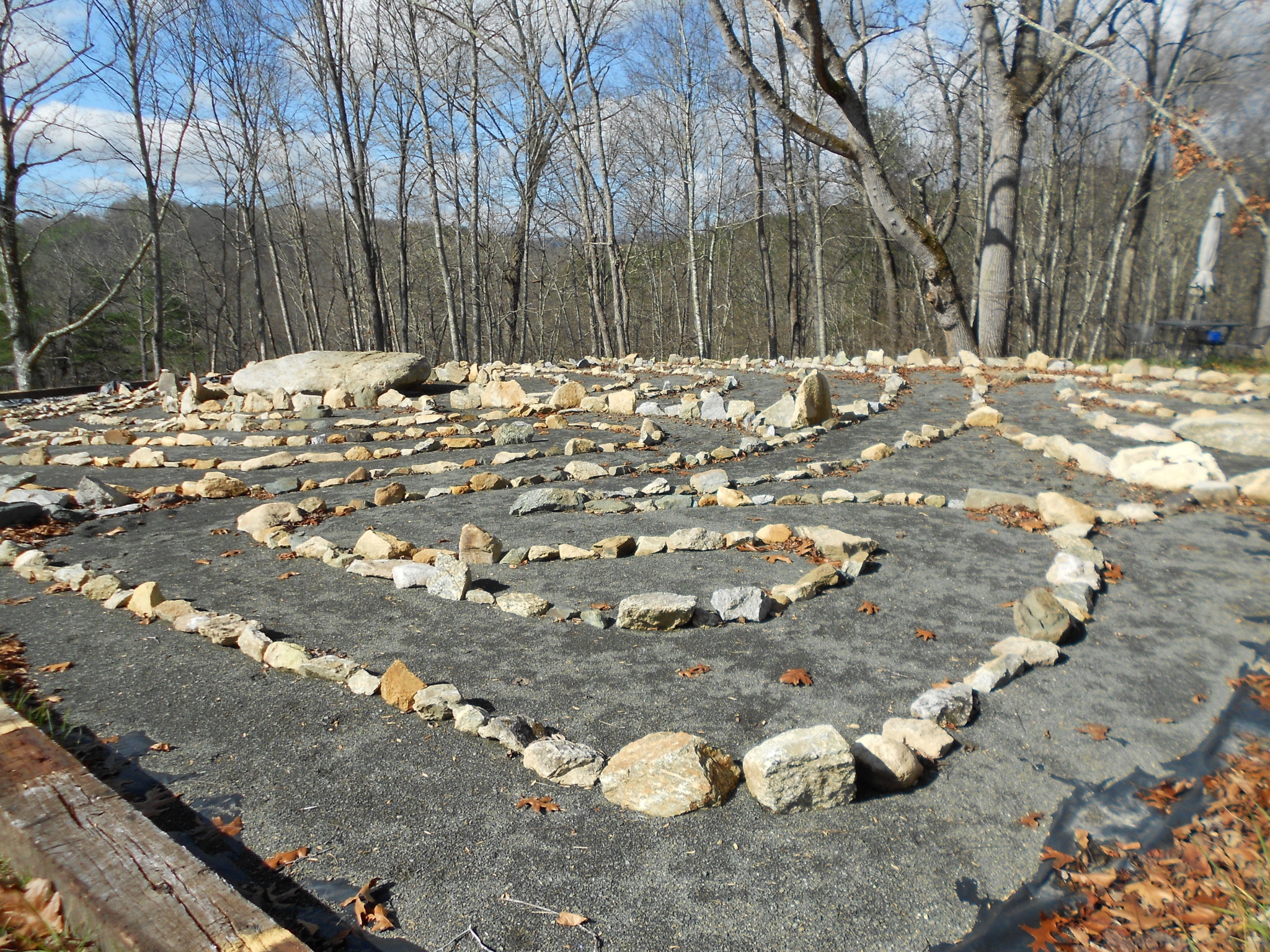 Stone labyrinth in a forest setting with leafless trees and blue sky.