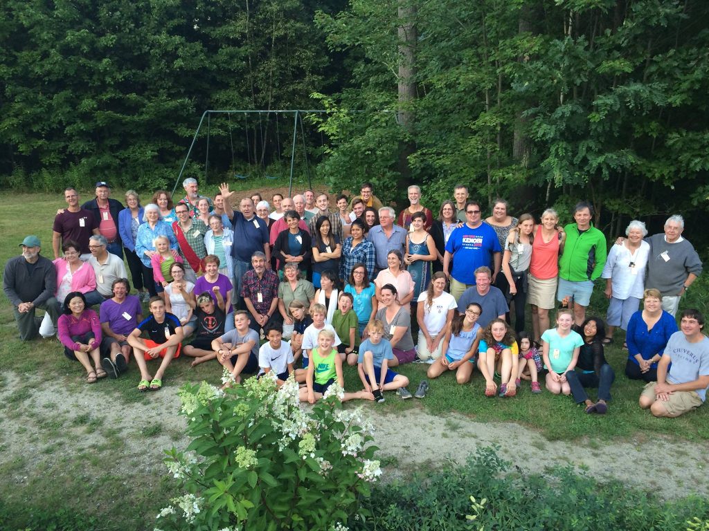 Large diverse group of people gathered outdoors in a park setting.