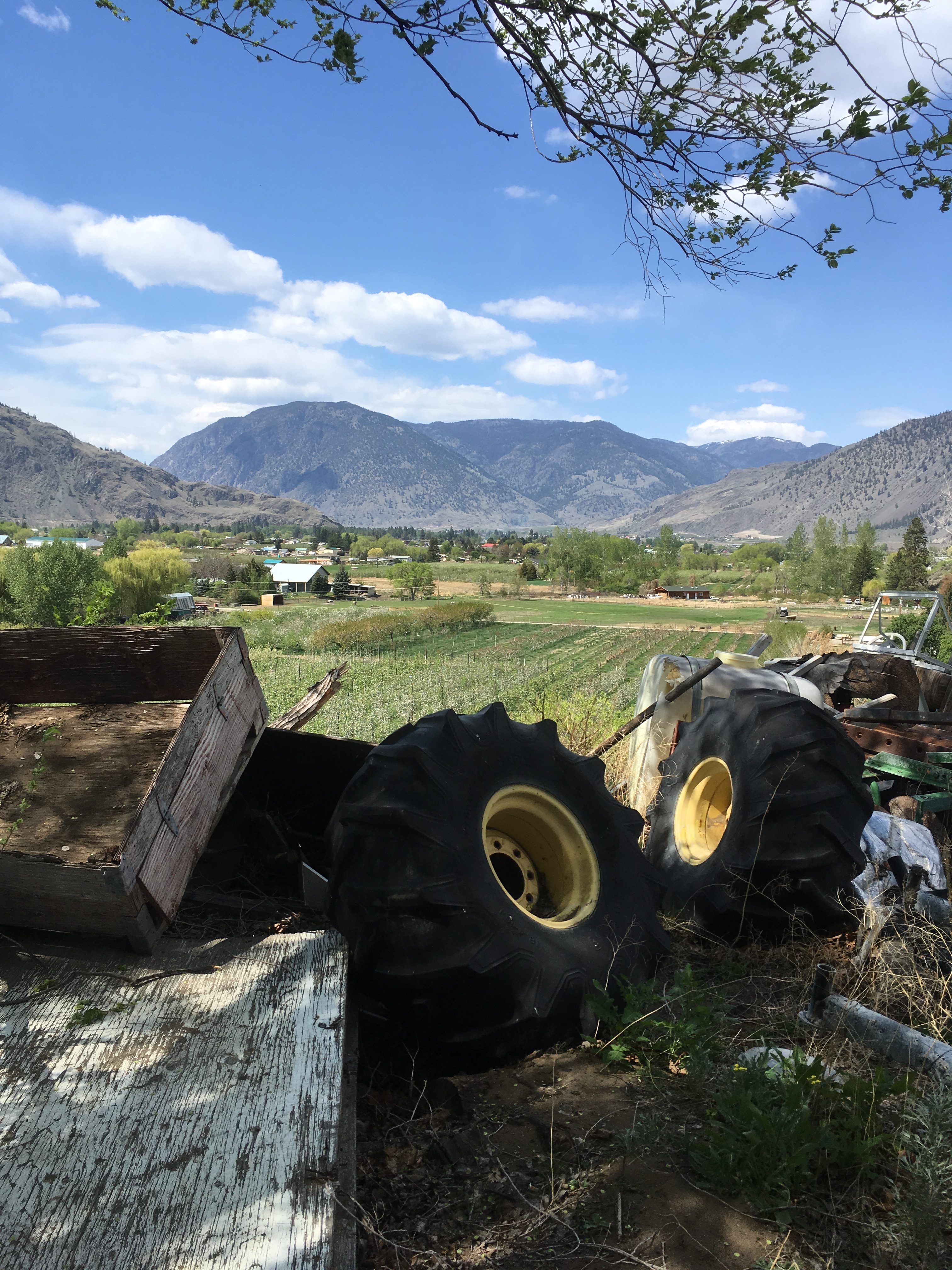 Scenic rural landscape with mountains, fields, and farm equipment under a blue sky.
