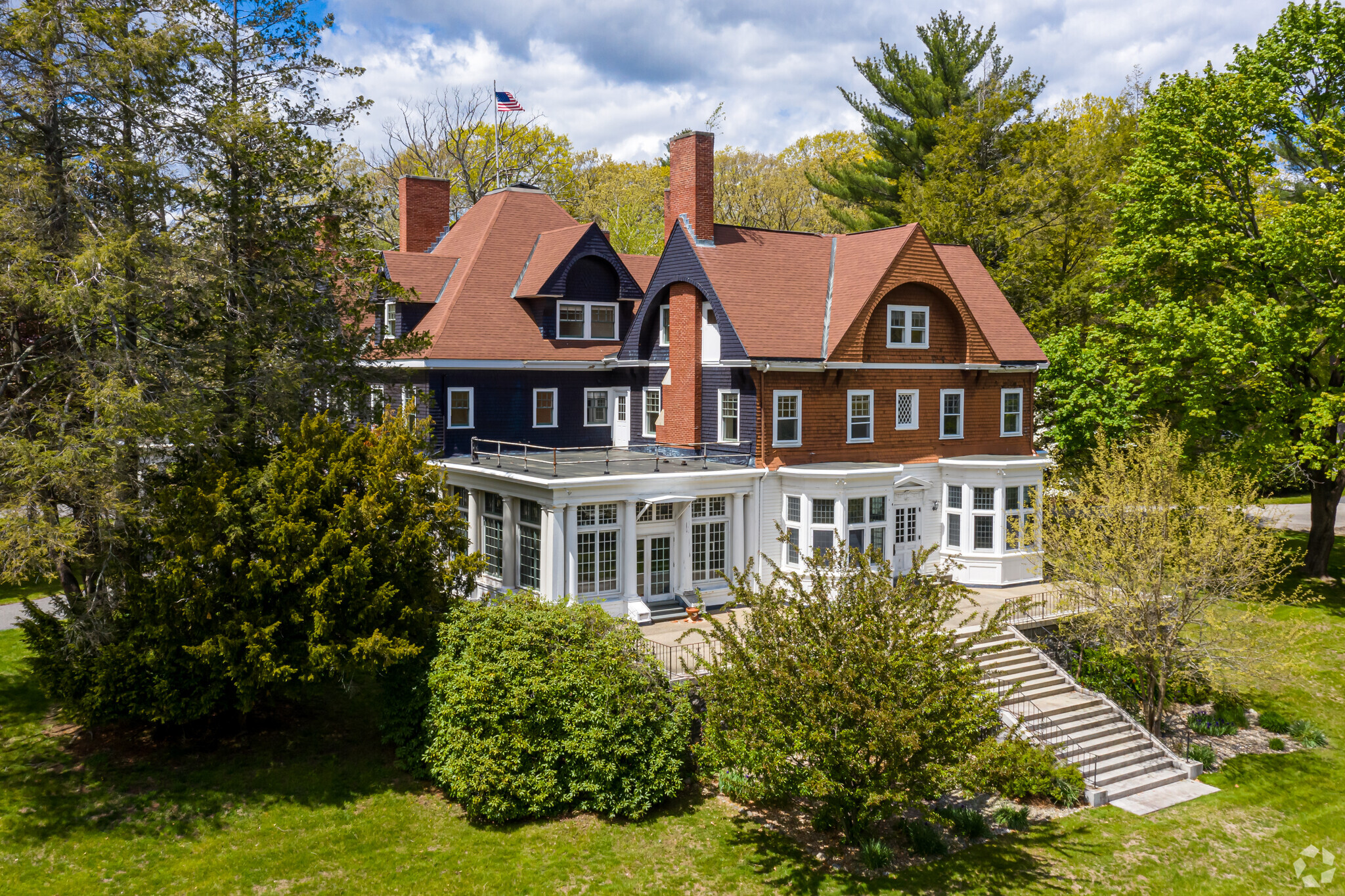 Historic house with a red roof surrounded by lush greenery and trees.