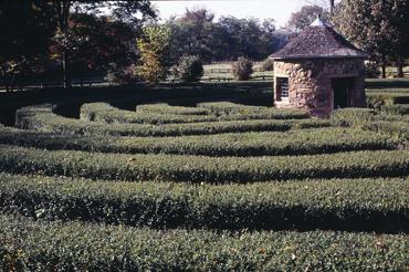 Manicured hedge maze with stone building in a park setting.