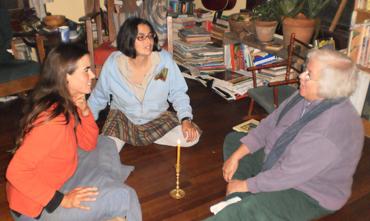 Three people engaged in a discussion at a wooden table in a cozy library.