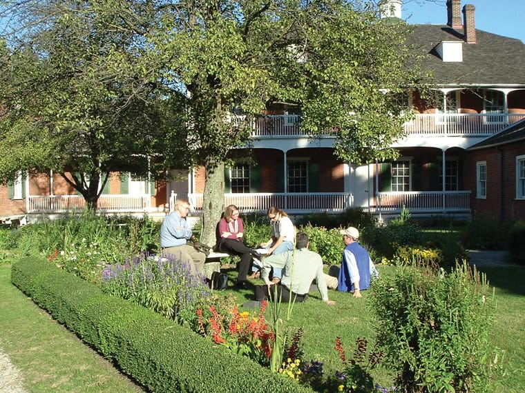 People sitting and talking in a garden with a large building in the background.