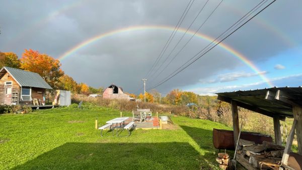 Rainbow over a farm with trees and buildings in the background.