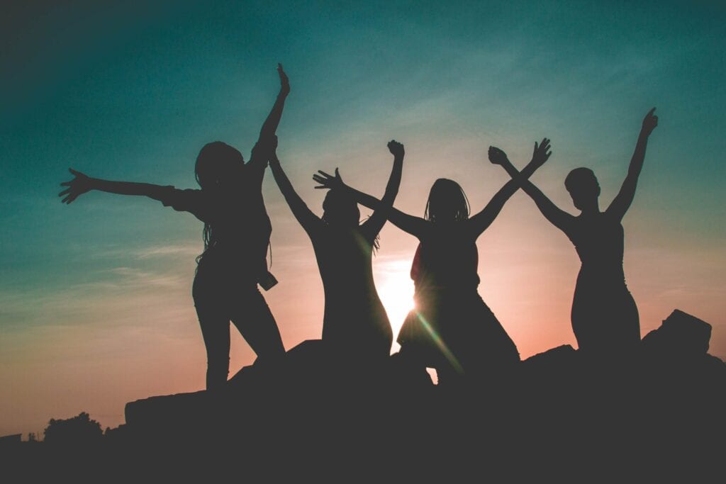 Silhouettes of four people celebrating at sunset with arms raised.