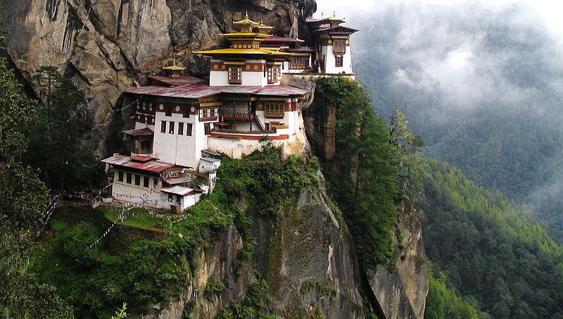 Traditional Bhutanese monastery built on a cliffside with lush green mountains.